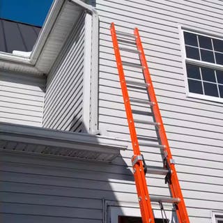 A red Louisville Ladder FE3228 28-Foot Fiberglass Extension Ladder Type IA leaning against a house.