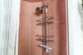 An empty OXO Aluminum 3-Tier Shower Caddy hanging from the arm of a showerhead