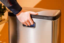 Close up of a person holding the handle located on the back of the rectangular step can.