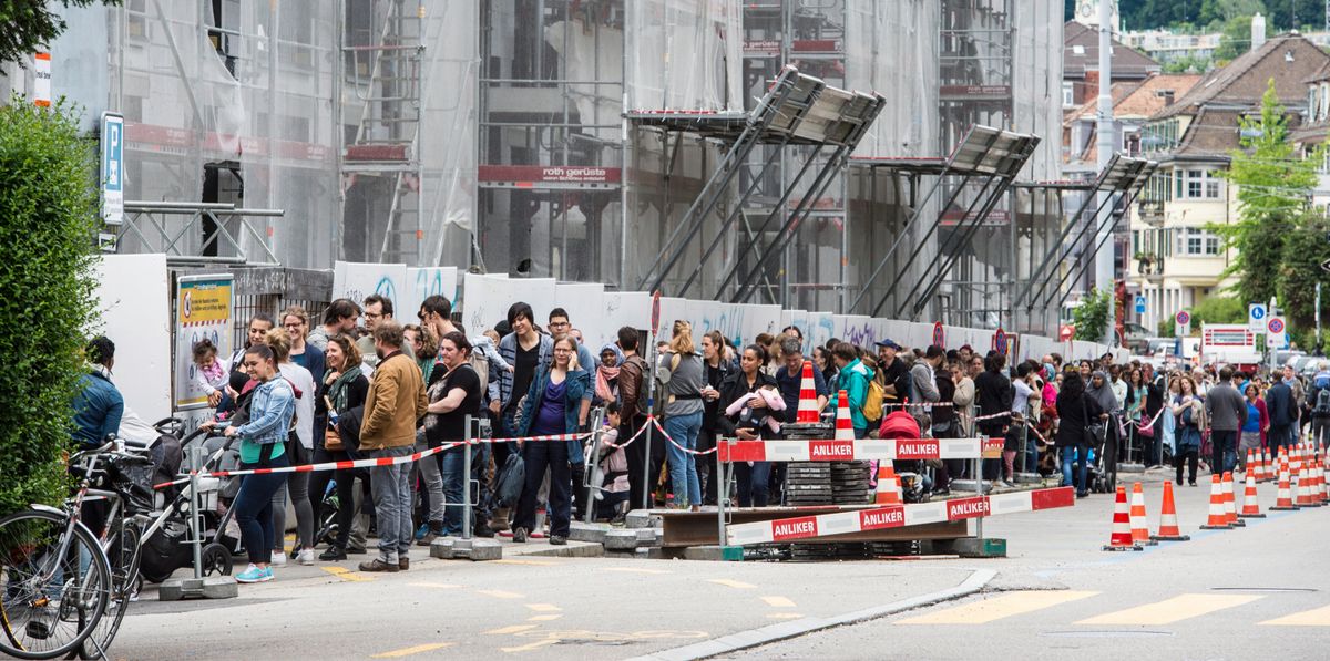 Eine lange Schlange von Menschen wartet vor einem im Bau befindlichen Wohngebäude in der Kronenwiese-Neubausiedlung in Zürich. Die meisten der Wartenden suchen Wohnungen zur Erstvermietung.