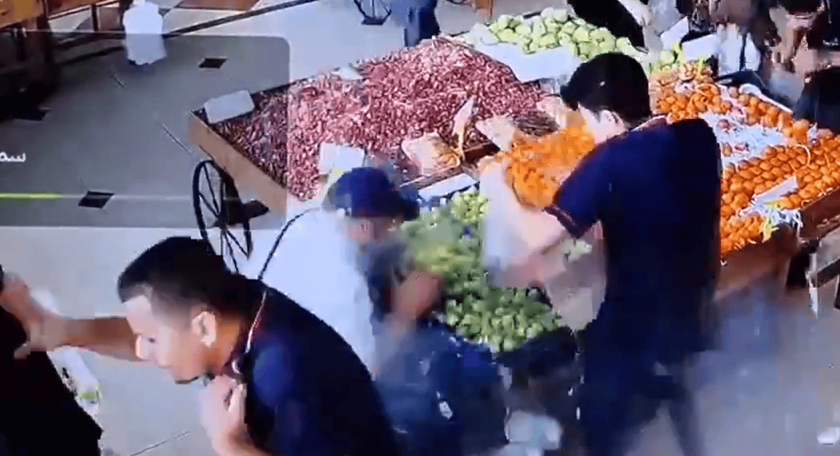 Ein belebter Marktstand mit verschiedenen Obstsorten wie Äpfel, Orangen und Paprika. Mehrere Personen sind dabei, Obst zu sortieren und zu verpacken.