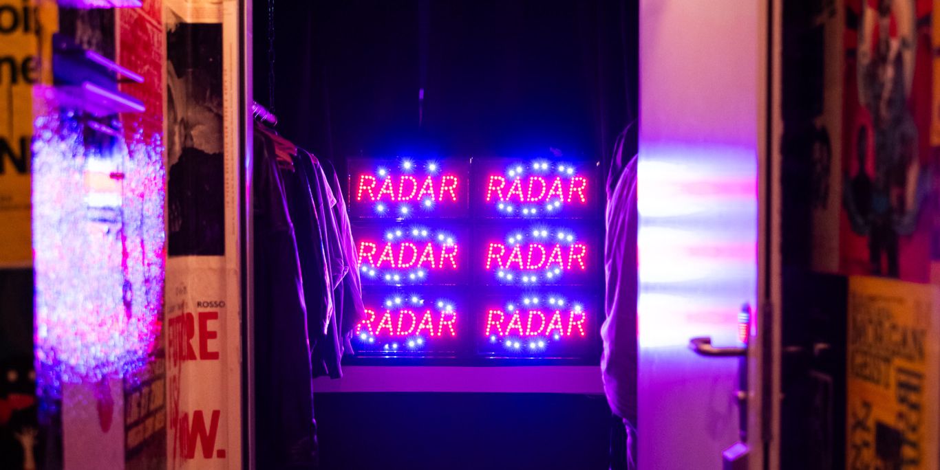 Neonbeleuchtetes 'Radar'-Schild in einem Raum mit Poster-bedeckten Wänden beim Radar Festival 2023.