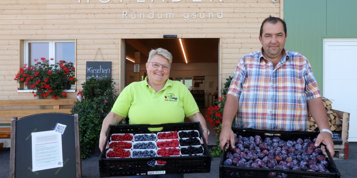 Astrid und Vincent Bütler vor ihrem Hofladen in Wädenswil, halten Körbe mit frischen Beeren und Pflaumen.