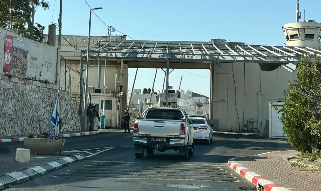 Einfahrt zu einem bewachten Checkpoint mit mehreren Fahrzeugen auf einer Strasse. Es gibt Mauerwerk und Stacheldrahtzäune sowie einen Wachturm.