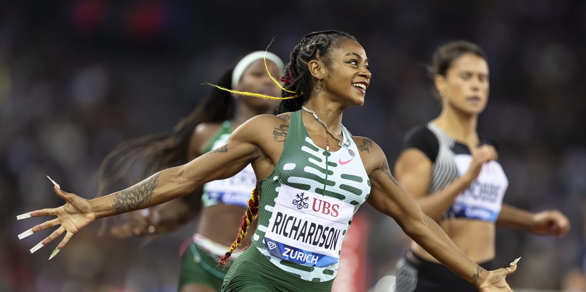 Läuferin jubelt bei einem Leichtathletikrennen im Stadion. Sie trägt ein grünes Trikot mit ihrem Namen 'Richardson'. Weitere Läuferinnen sind im Hintergrund zu sehen.