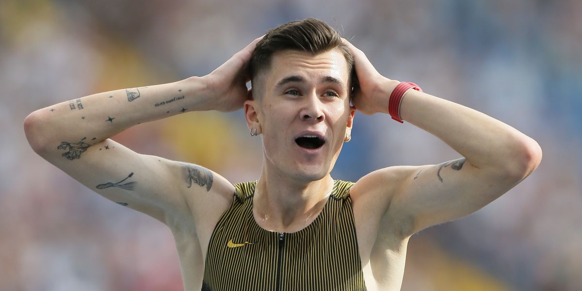 Ein männlicher Sportler mit Tattoos auf den Armen hält sich überrascht den Kopf bei einem Leichtathletik-Event.