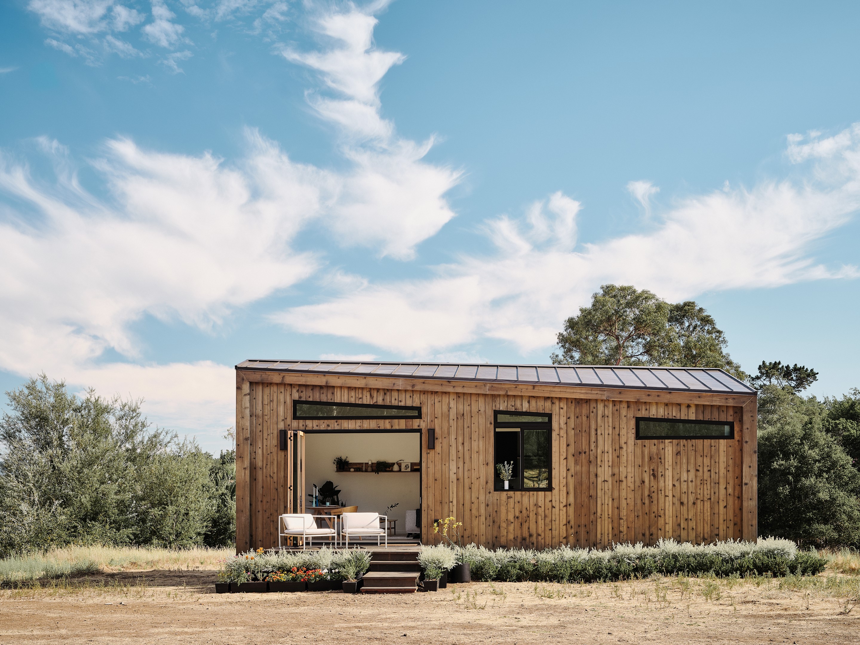 A small wood-clad prefab home with slanted roof sits on grassy plot.