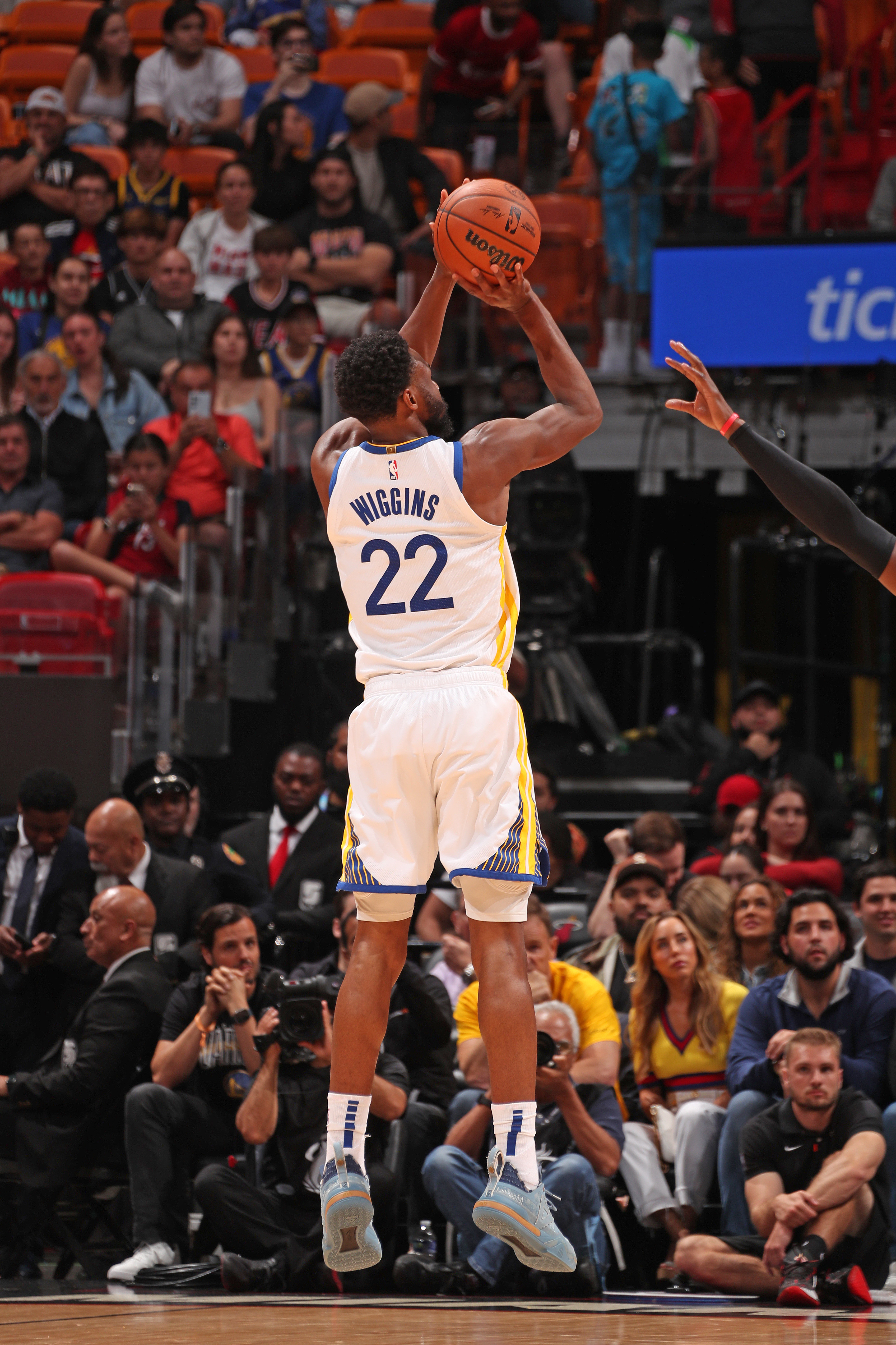 Andrew Wiggins is about to shoot the ball during the game against the Miami Heat at Kaseya Center. An opposing player’s arm reaches to block him. The Warriors are wearing their white jerseys.