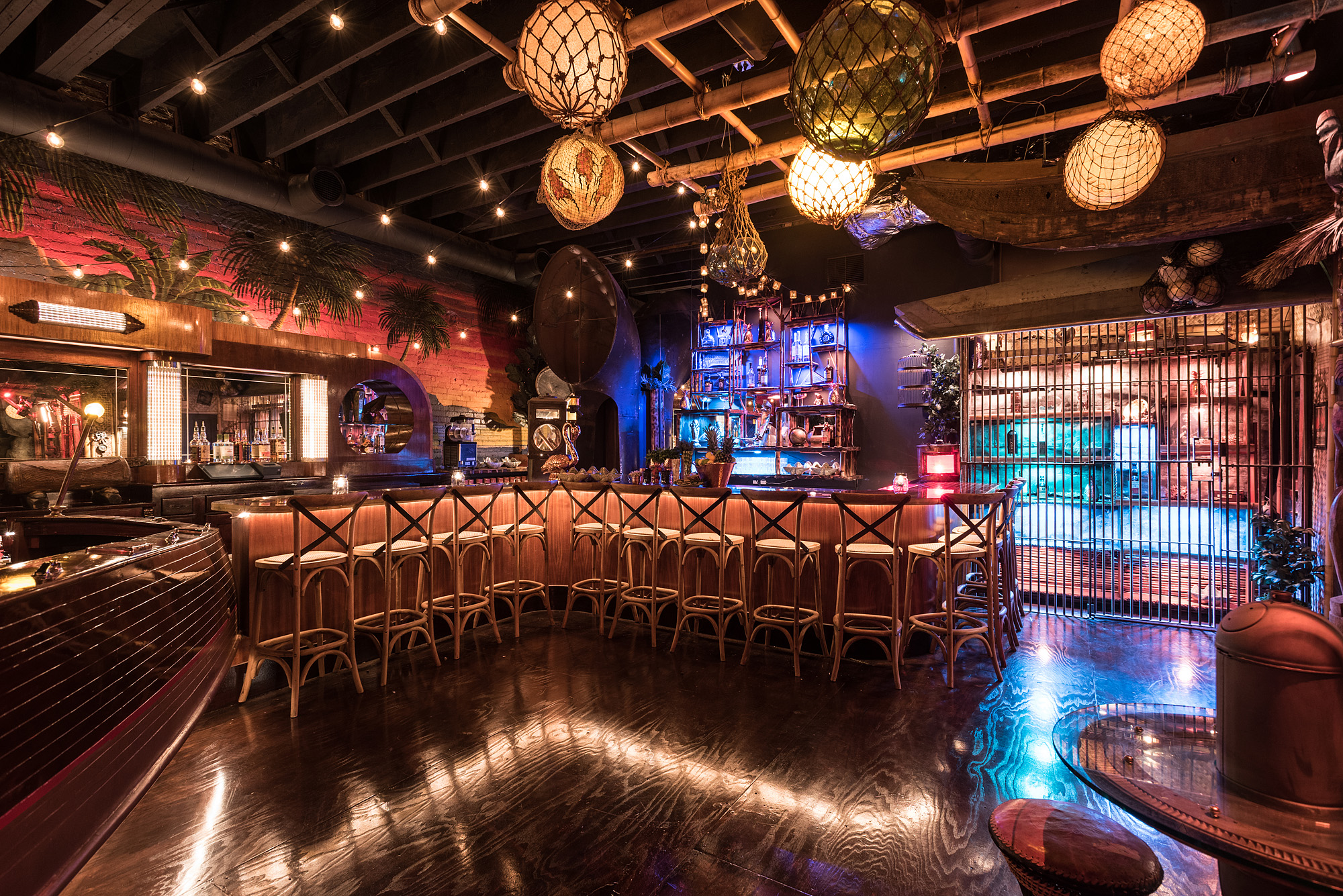 A Tiki-themed bar with hanging lights, wooden barstools, bars, colorful murals, and tiki decor at Clifton’s Republic in Downtown Los Angeles.