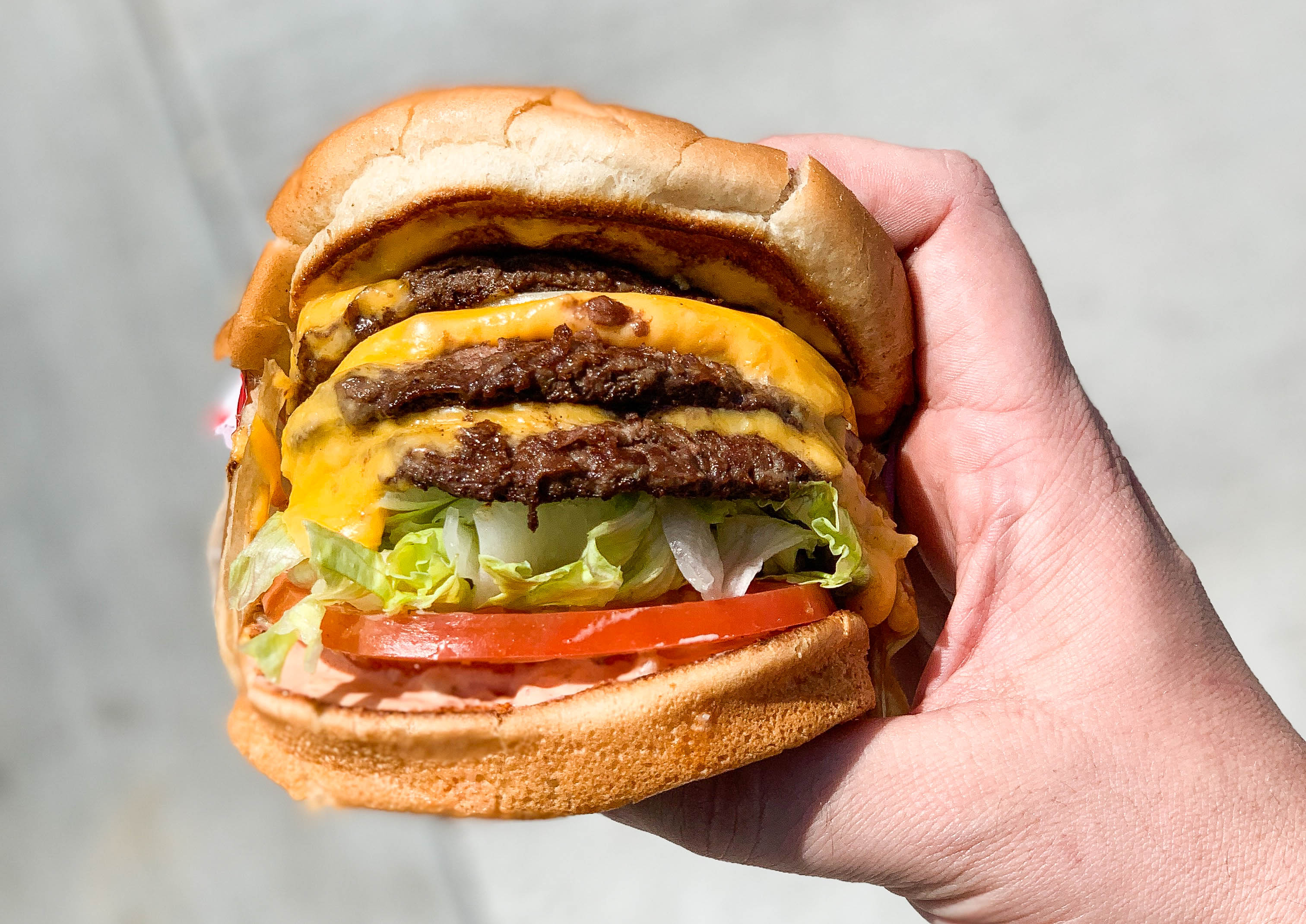 A hand holds a cheese burger from chain restaurant In-N-Out.