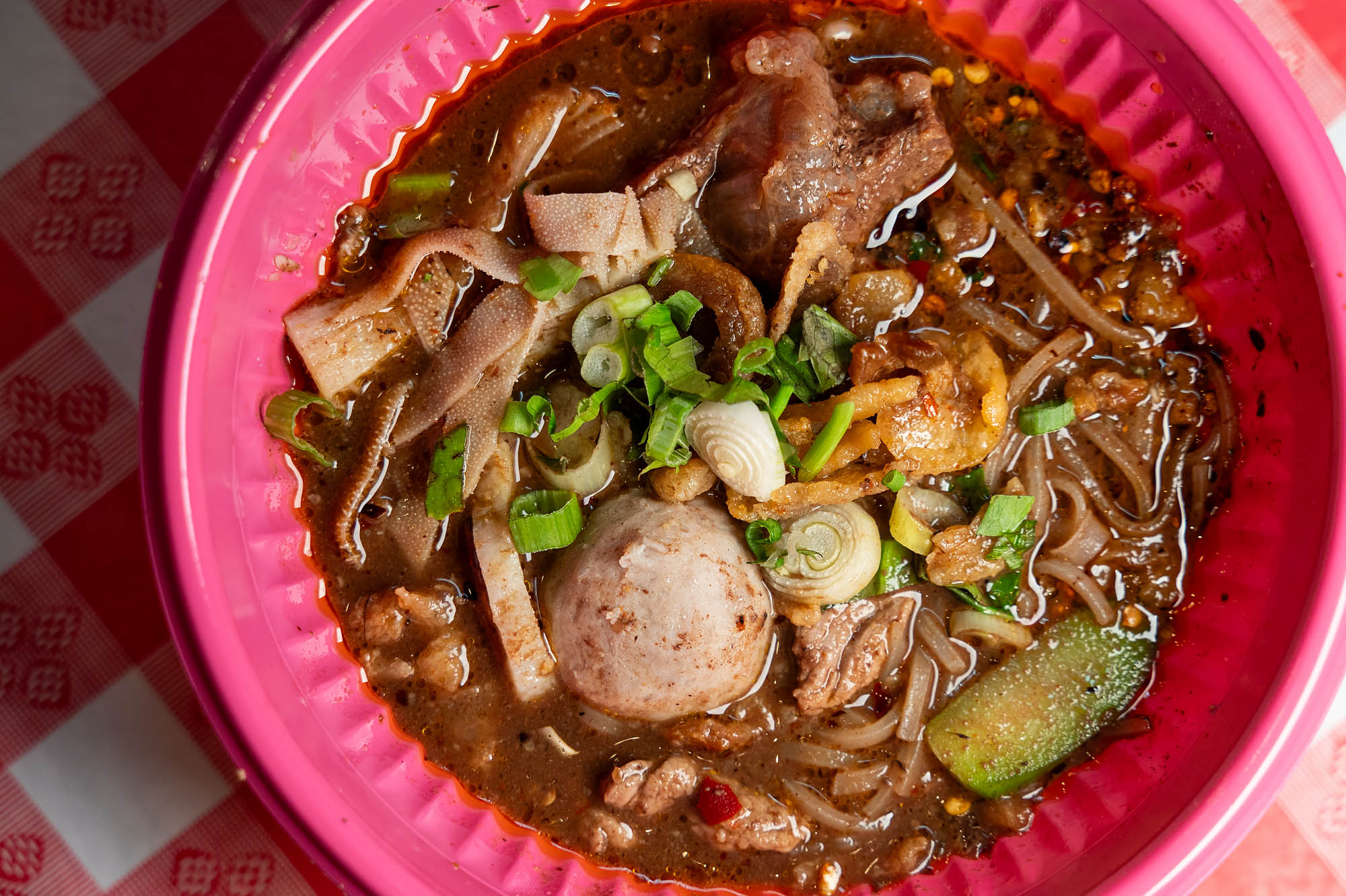 Boat noodle soup served in a pink plastic bowl set on a checkered red and white tablecloth at Mae Malai on Hollywood Boulevard.