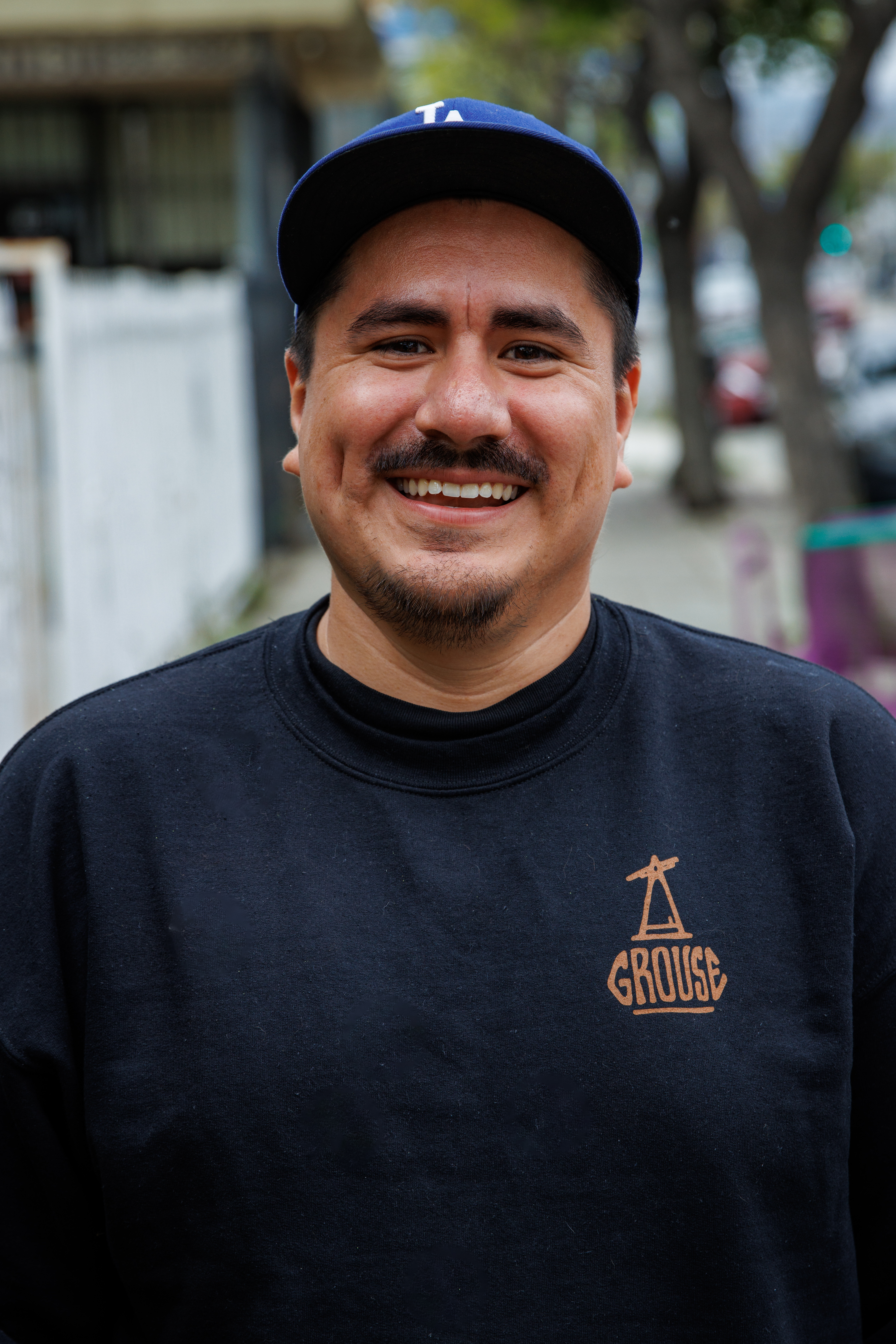 Chef Jimmy Reyes with a mustache wearing a Dodgers hat and a black sweatshirt. 