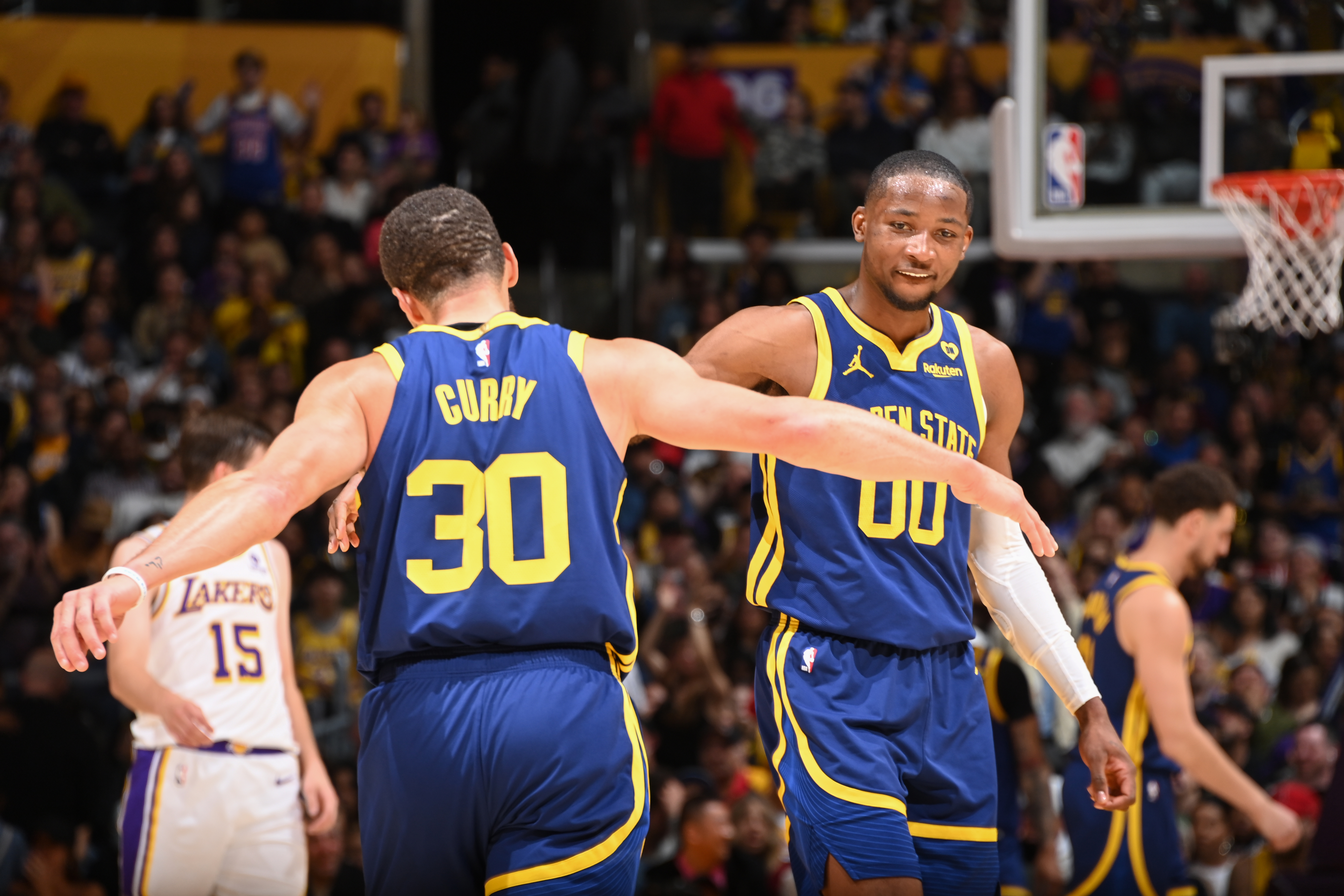 View from behind Steph Curry, and in front of Jonathan Kuminga, as they reach out to slap hands. 