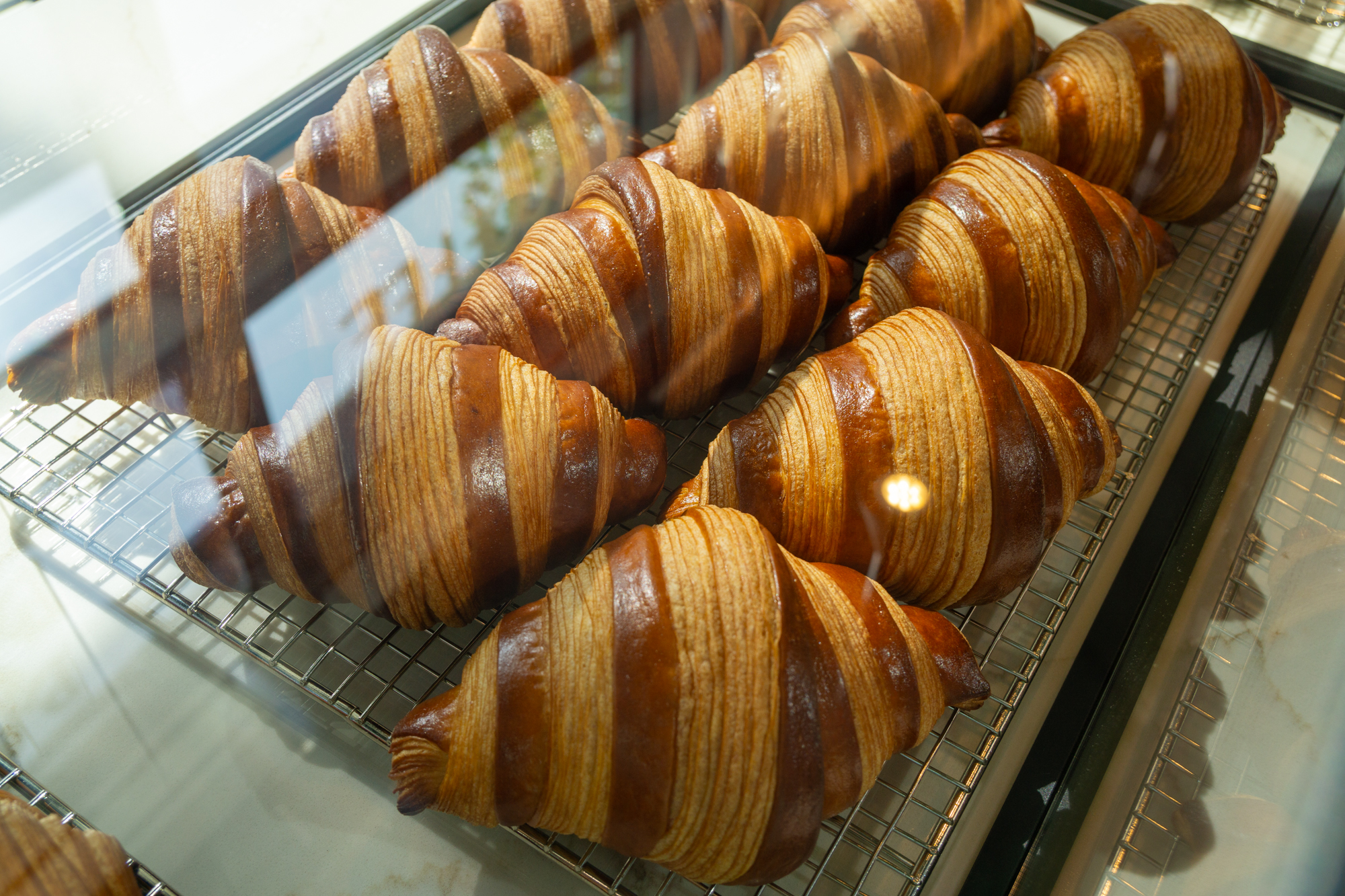 Golden croissants at Mr. T Cafe in Hollywood on a cooling rack behind a glass case.