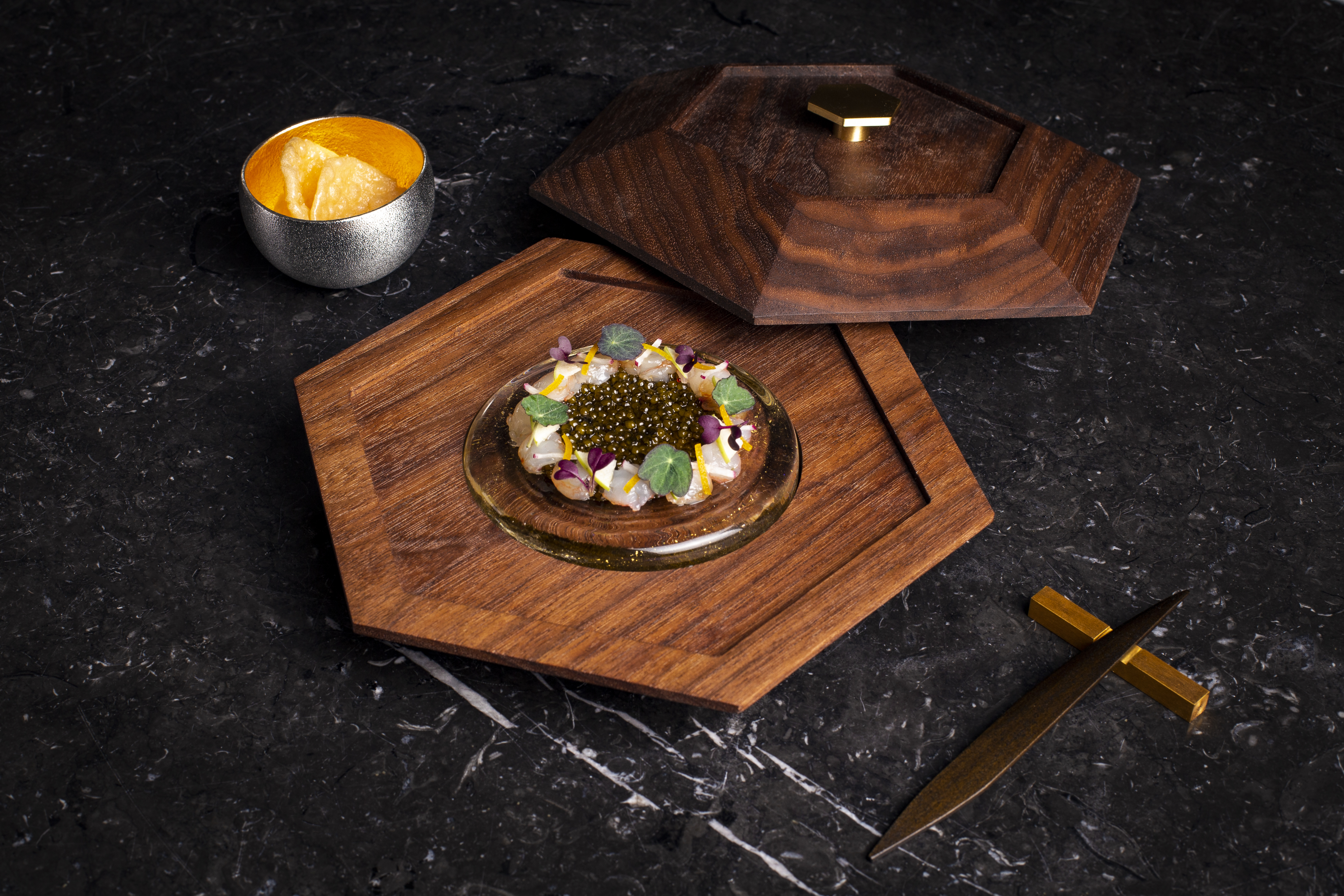 A circle of thinly sliced spot prawn around a quenelle of caviar on a wooden plate.