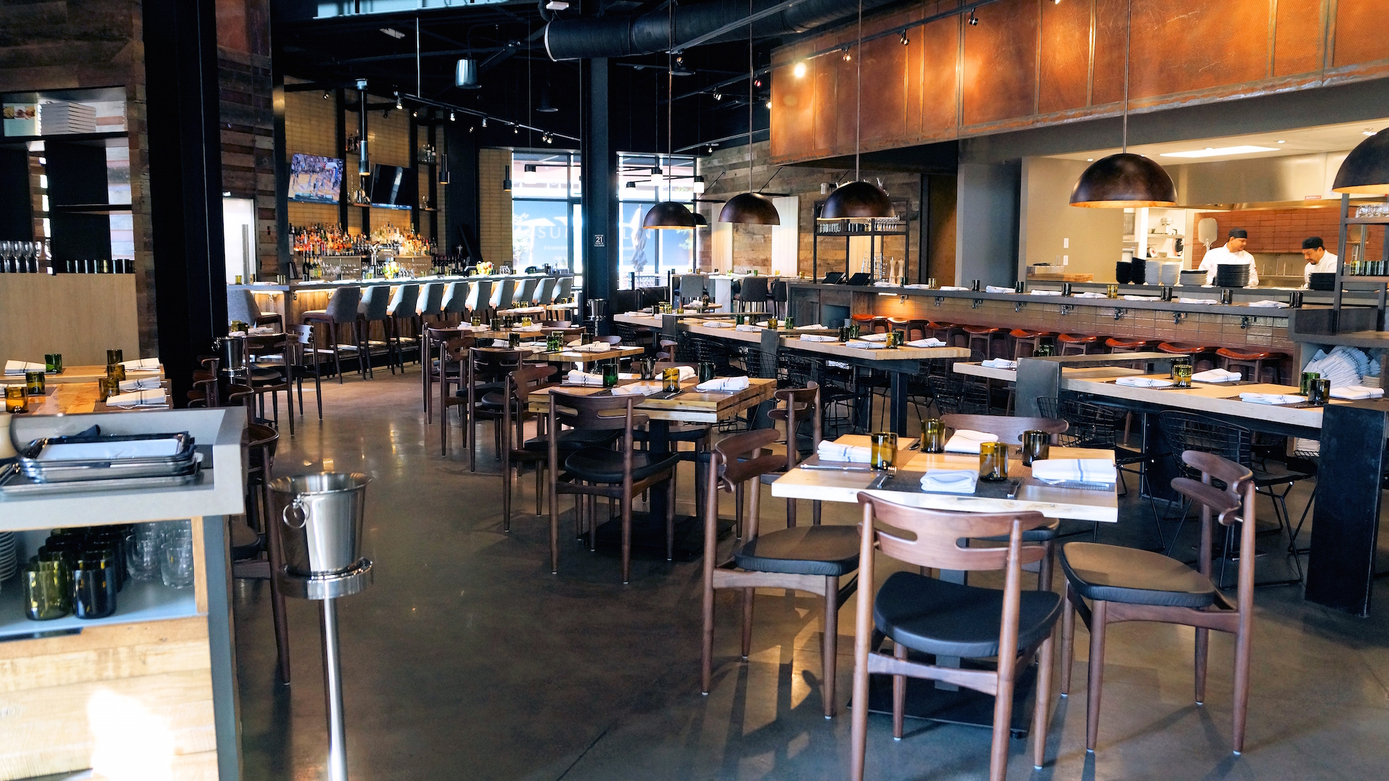 Wolfgang Puck Bar &amp; Grill interior with high tops and an open kitchen.