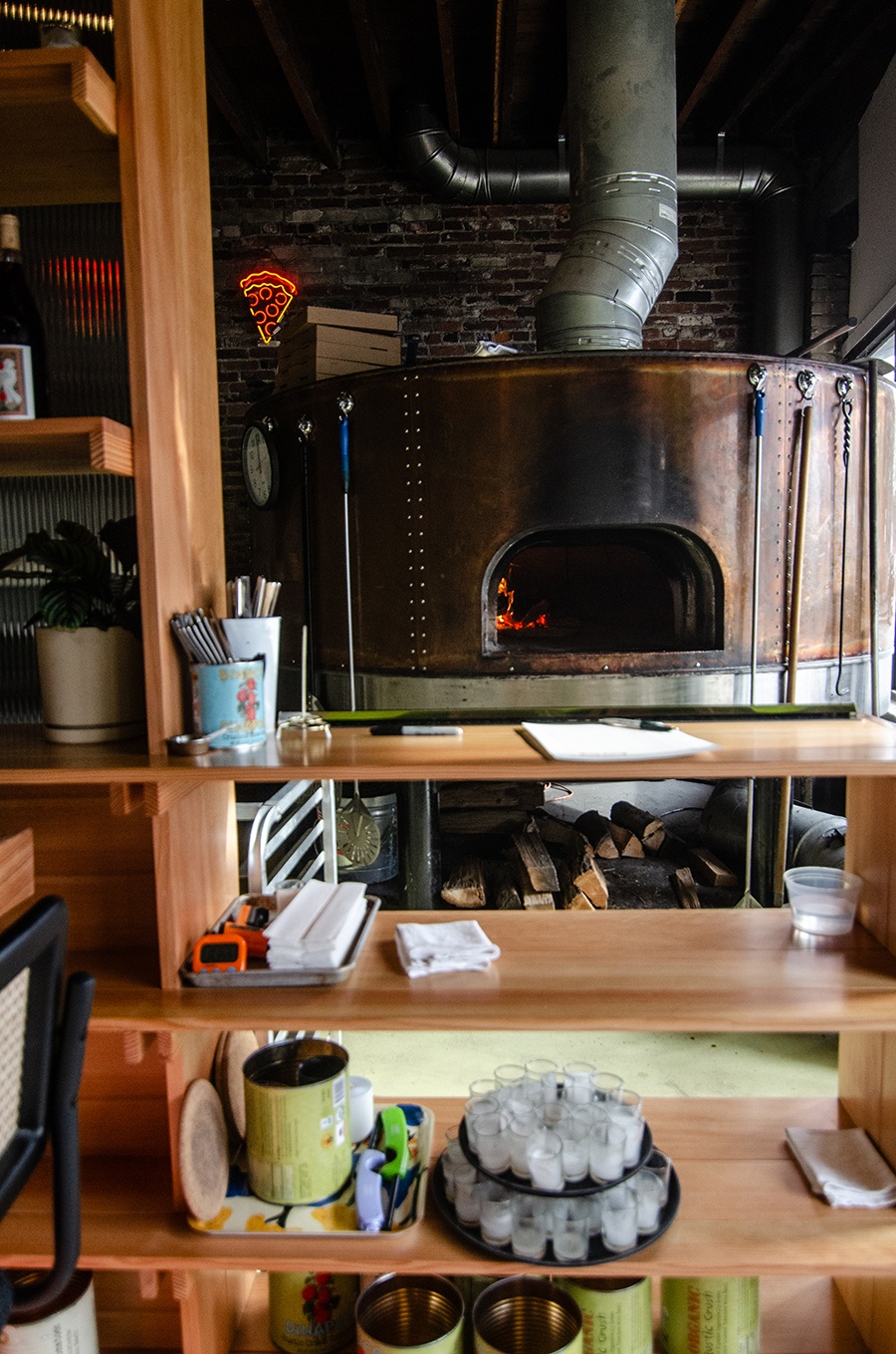 A shiny bronze pizza oven sits inside a restaurant in front of a brick wall.