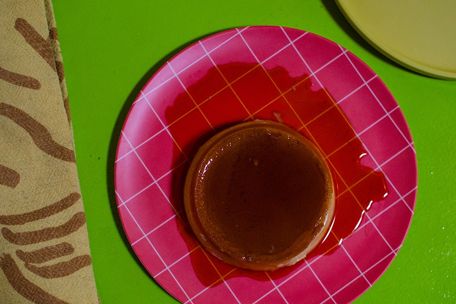 Overhead view of flan on a pink plate on a green surface.