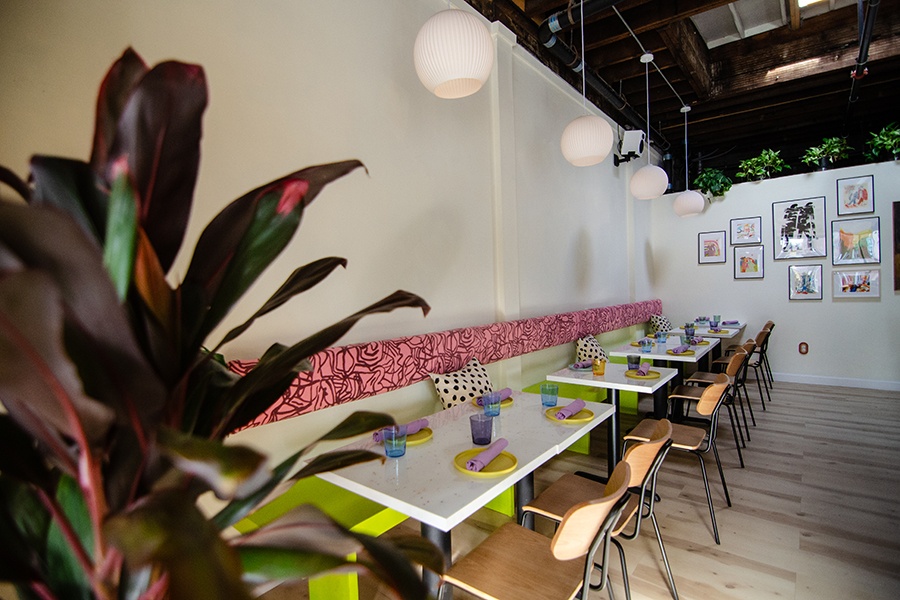 A restaurant dining room features polka dot pillows on a green bench with a pink patterned cushion.