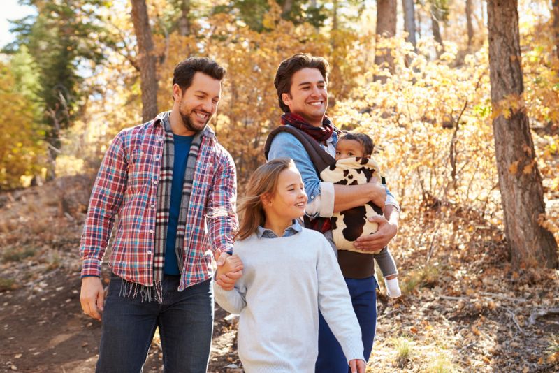 Una pareja de dos hombres gay con dos niños adoptados caminando felices en el bosque.