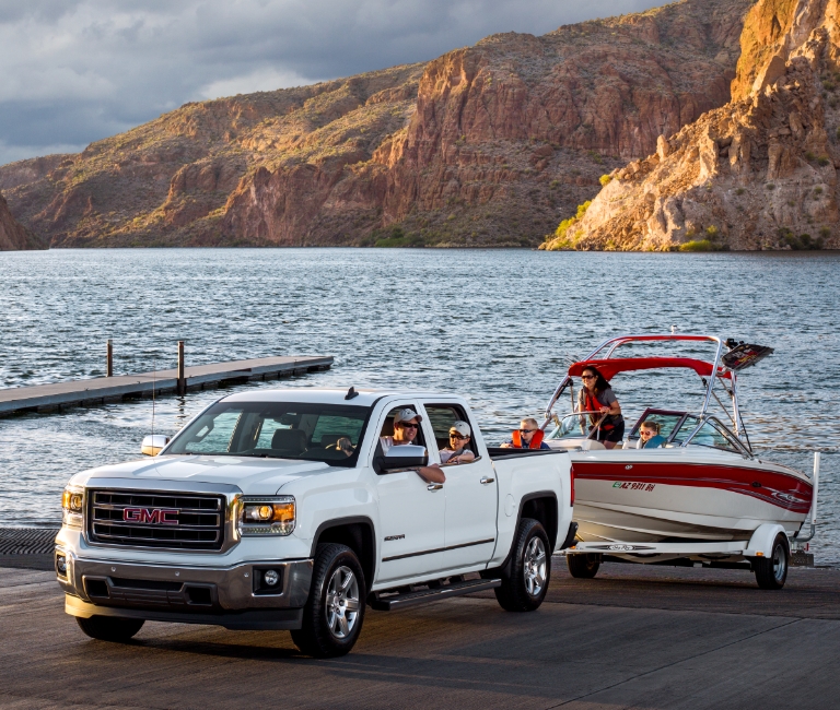 A family in a pick-up truck pulling a boat out of a lake and onto a trailer