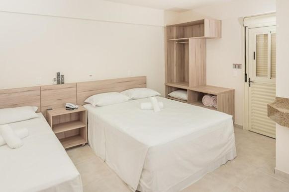 um quarto branco com uma grande cama branca e prateleiras em Hotel Dois H em Joinville