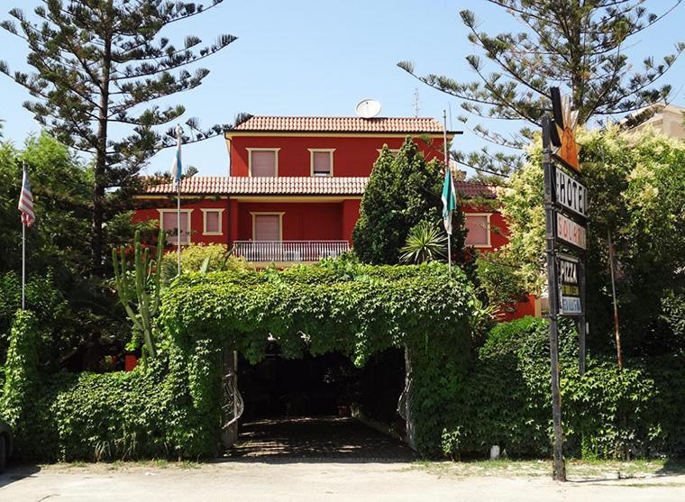 uma casa vermelha com uma cerca em frente a um edifício em Hotel Ristorante Solari em Briatico