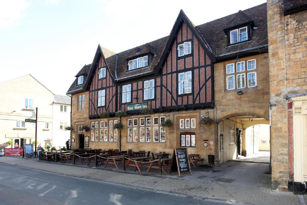 Half Moon, Sherborne by Marston's Inns في شيربورن: مبنى امامه طاولات وكراسي