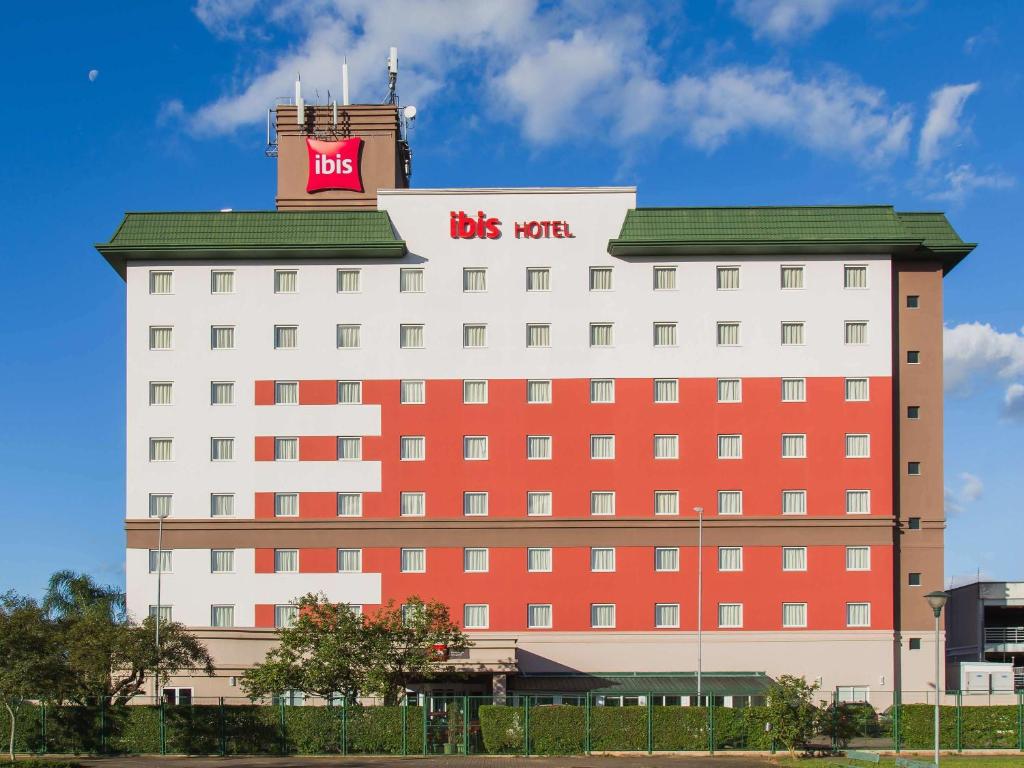 un grande edificio rosso e bianco con un cartello di autobus sopra di ibis Porto Alegre Aeroporto a Porto Alegre