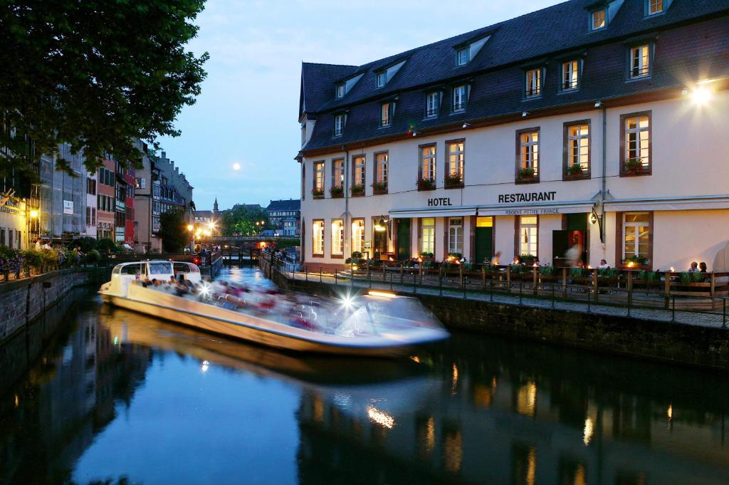 a boat traveling down a river in front of buildings at Hotel & Spa REGENT PETITE FRANCE in Strasbourg