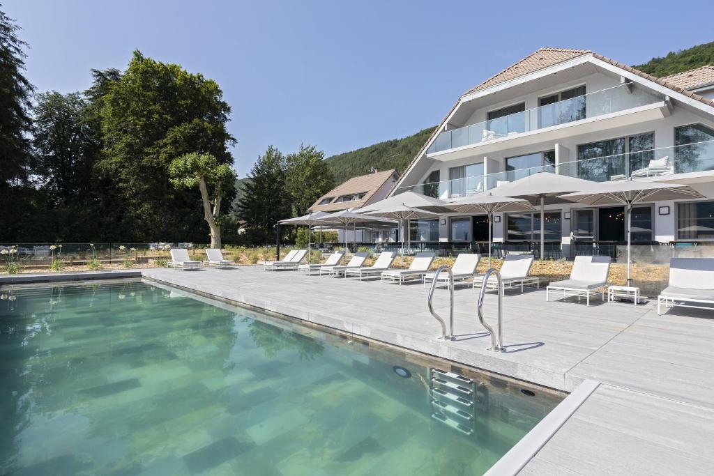 einem Pool mit Stühlen und Sonnenschirmen vor einem Gebäude in der Unterkunft Black Bass Hotel in Sévrier