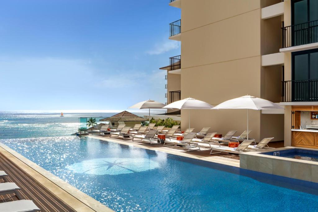 a hotel swimming pool with chairs and the ocean at Halepuna Waikiki by Halekulani in Honolulu