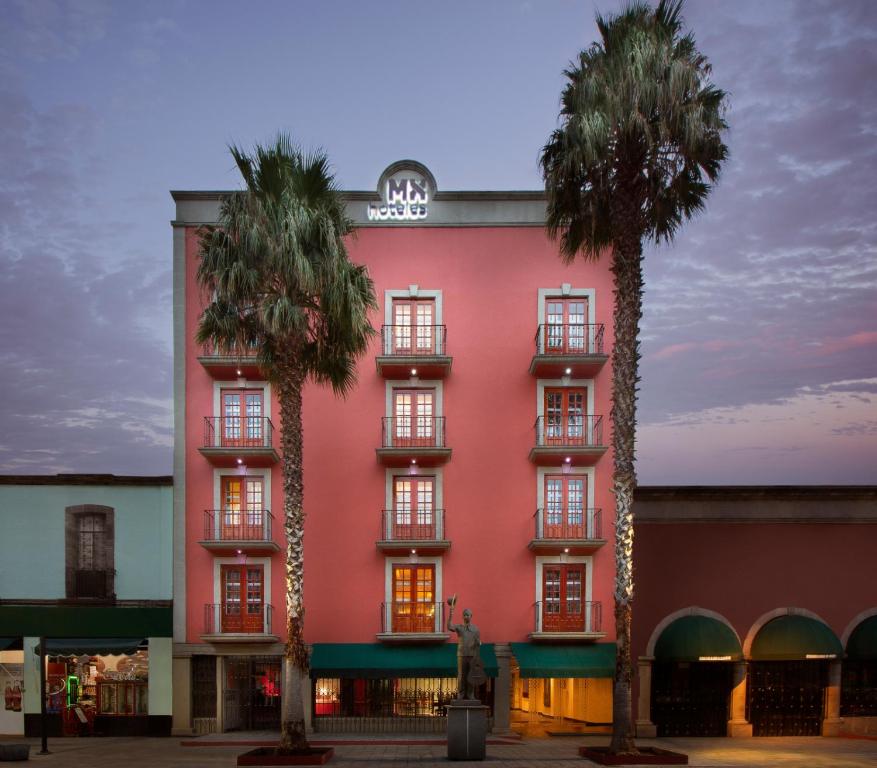 a pink building with two palm trees in front of it at Hotel MX garibaldi in Mexico City