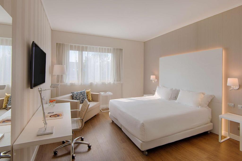 een hotelkamer met een wit bed en een bank bij NH Torino Centro in Turijn