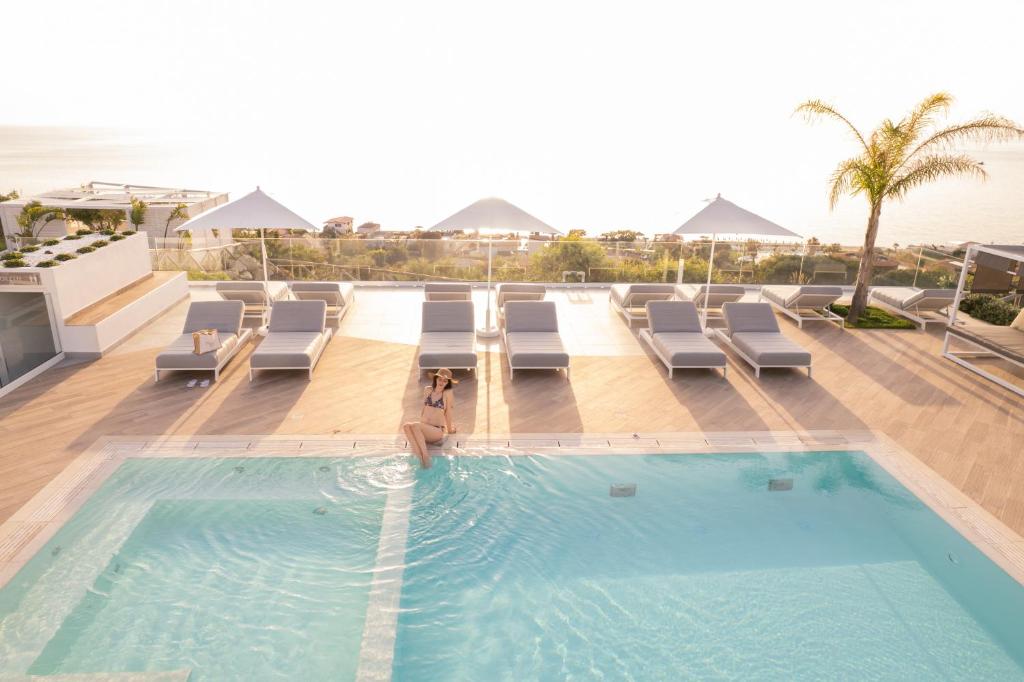 a swimming pool with lounge chairs and the ocean at Midenza Seaside & Nature Retreat in Capo Vaticano