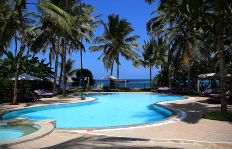 uma grande piscina com palmeiras e o oceano em Turtle Bay Beach Club em Watamu