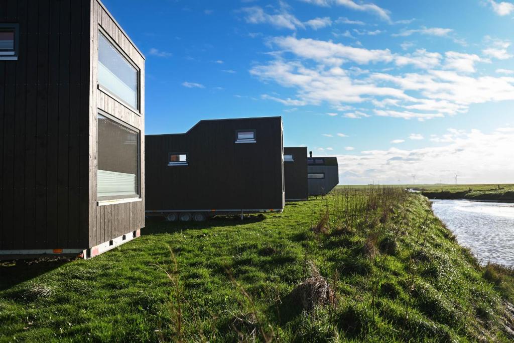 una fila de casas negras a orillas de un río en Tiny House Nature 14 Zur Meerseite - Green Tiny Village Harlesiel, en Carolinensiel