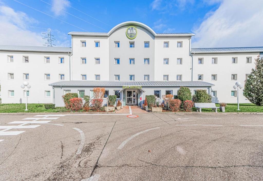 un parking vide en face d'un grand bâtiment blanc dans l'établissement B&B HOTEL Strasbourg Nord Mundolsheim, à Mundolsheim