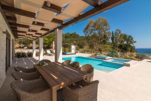 eine Terrasse mit einem Holztisch und Stühlen sowie einem Pool in der Unterkunft Porto Vasilikos Villas in Xirokástellon