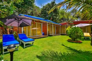 une maison avec une cour dotée de chaises et d'un parasol dans l'établissement Zulu Land cottages - near Curlies beach shack and shiva valley - Anjuna beach, à Anjuna