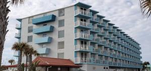 a tall white building with blue balconies and palm trees at Fountain Beach Resort - Daytona Beach in Daytona Beach