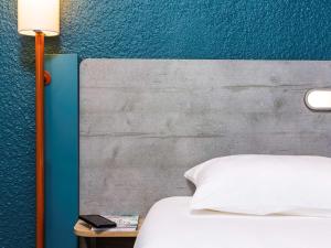 a bed with a white pillow and a table with a lamp at Ibis Budget Strasbourg Centre Gare in Strasbourg