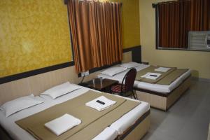 a room with two beds and a chair in it at Hotel Sai Vishwa in Shirdi