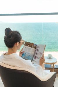 une femme assise sur une chaise en lisant un livre dans l'établissement La Vague Hotel, à Nha Trang