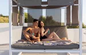 a man and woman sitting on a bed with drinks at Midenza Seaside & Nature Retreat in Capo Vaticano