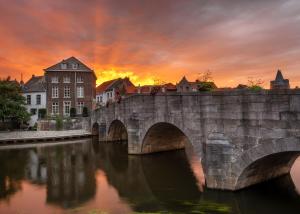 een stenen brug over een rivier met een zonsondergang bij Grand Hotel Valies in Roermond