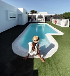 a woman in a hat sitting next to a swimming pool at Hyde Park Lane Villas in Puerto del Carmen