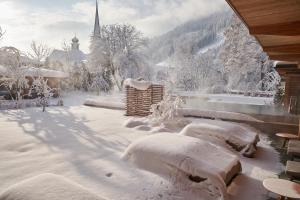 a yard covered in snow with a church in the background at MalisGarten Green Spa Hotel in Zell am Ziller