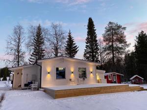 une petite maison blanche dans la neige avec des arbres dans l'établissement Modern Lapland Cottage with Outdoor Sauna & BBQ Hut, à Slagnäs