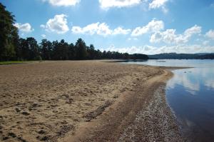 a sandy beach with trees and water and clouds at Hamresanden Resort in Kristiansand